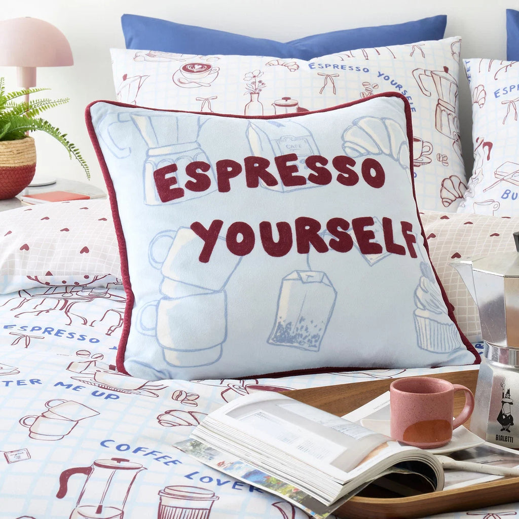 Decorative pillow with 'Espresso Yourself' text on a bed with coffee-themed bedding.